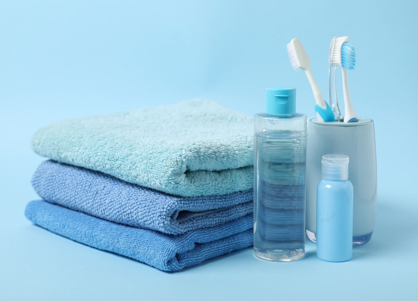 Toothbrushes, mouthwash bottle, and folded towels arranged on a light blue background